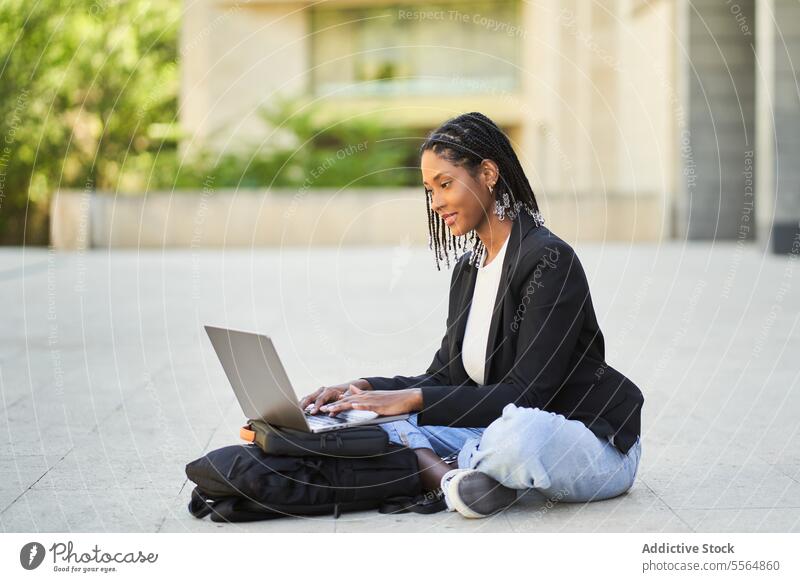 African American woman sitting on floor with laptop against blurred background of building street businesswoman modern work netbook entrepreneur casual using