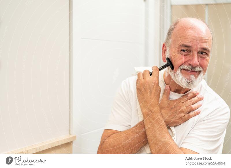 Delighted senior man shaving in bathroom shave razor beard grooming shaver routine daily self care male hygiene foam gray hair procedure morning appearance