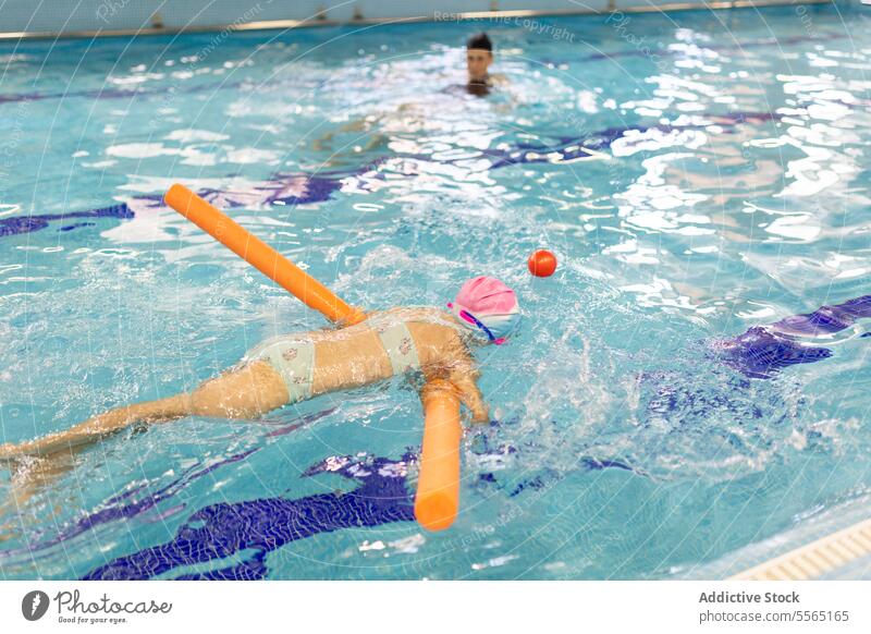 Preschooler girl practices swimming with instructor's supervision pool indoor swimmer preschooler noodle orange float safety water training lesson buoyancy