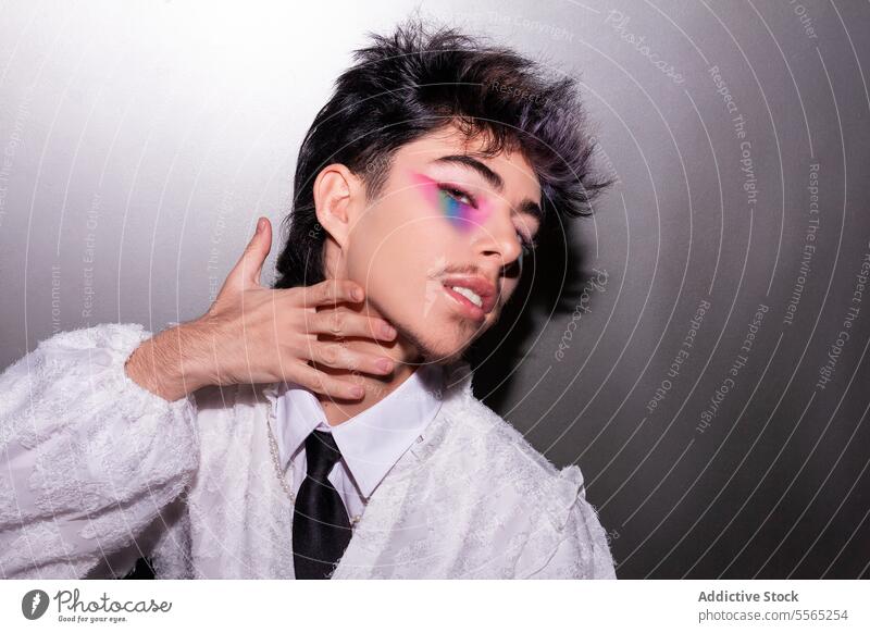 Man in profile with vivid rainbow makeup man eye hair tousled hand neck backdrop neutral side fashion style contemporary face close-up color design elegant