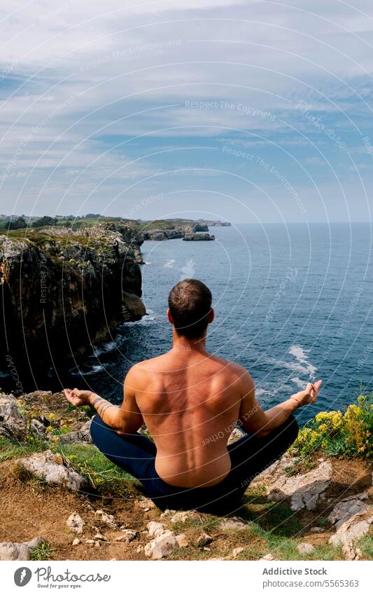 Man meditating on rugged coastline with expansive sea view. man meditation rocky cliff serene sky horizon yoga relaxation nature outdoors tranquil sitting calm