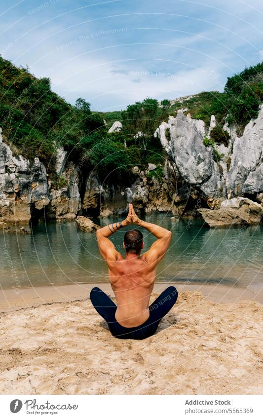 man doing Meditation at tranquil lagoon setting meditation lotus position beach cliffs greenery sky clouds water nature serenity peace relaxation focus calm