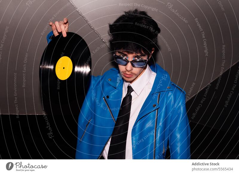 Retro-styled man with vinyl record in the dark stylish glasses lounging blue jacket leather pants retro music fashion 80s ambiance vintage youth subculture