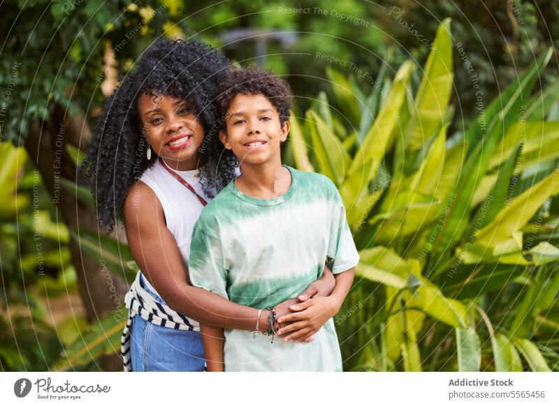 Joyful embrace Mum and son in a tropical setting woman boy plants joy smile curly hair love family affection green shirt bond happiness connection mother