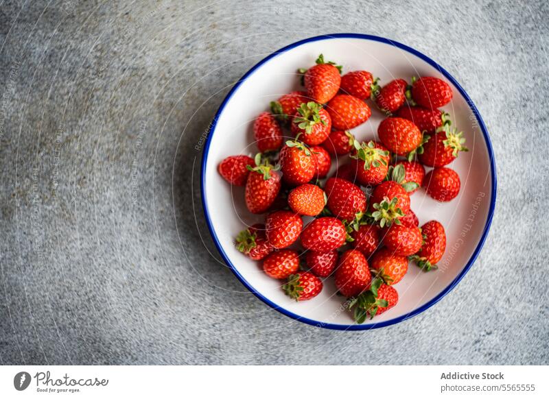 Organic strawberries in a plate against a grey background. Strawberry organic red fruit fresh ripe natural food healthy sweet juicy vegetarian vegan white blue