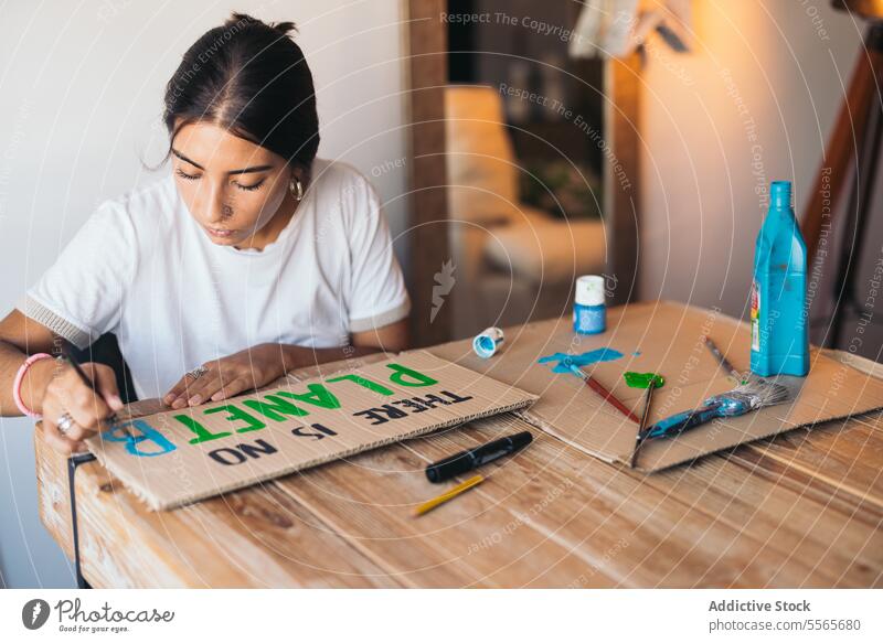 Woman painting a poster about the environment woman text earth cardboard table room cozy supplies design brush home wood sit joy creativity indoor leisure