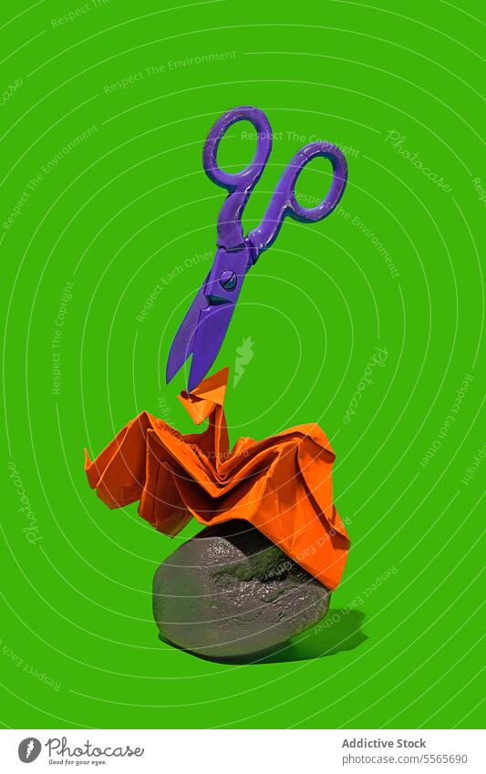 Scissors over paper on rock against a green background. Rock, paper and scissor minimalist concept purple orange hover craft fold art object texture tool cut