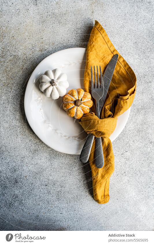 Decorative pumpkin plate setting decoration fork knife napkin mustard ceramic silver texture gray surface autumn festive tableware dining design fall