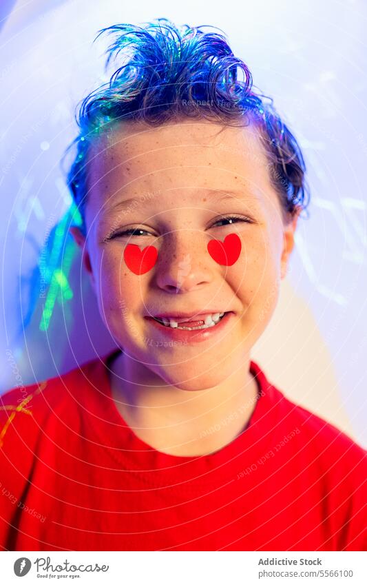 Calm boy with heart stickers on cheeks and abstract red patterns Boy curly hair calm gaze red shirt white background emotion child young expression love serene