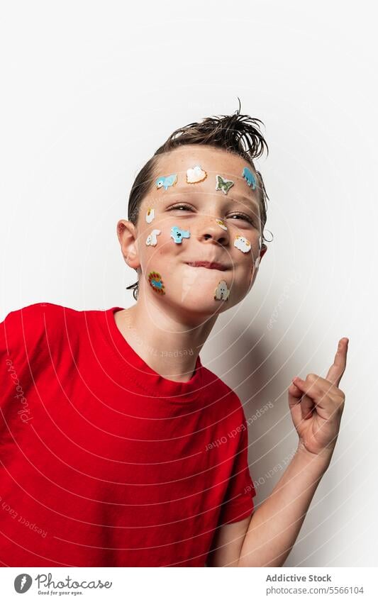Boy with animal stickers on face boy wet hair red shirt white background child playful fun portrait close-up expression cute youth innocence style modern