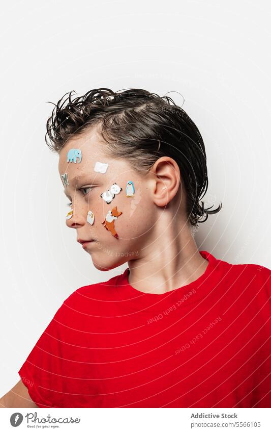 Boy with animal stickers on face boy wet hair red shirt white background child playful fun portrait close-up expression cute youth innocence style modern