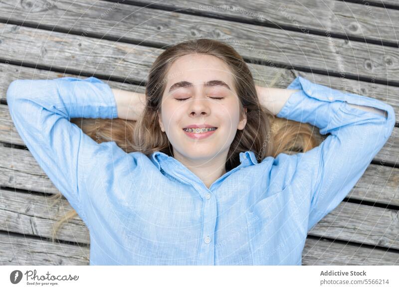Top view of happy student young female with braces lying on a wooden background. girl gen-z relaxing smiling close-up top view arms fun bench woman calm mental