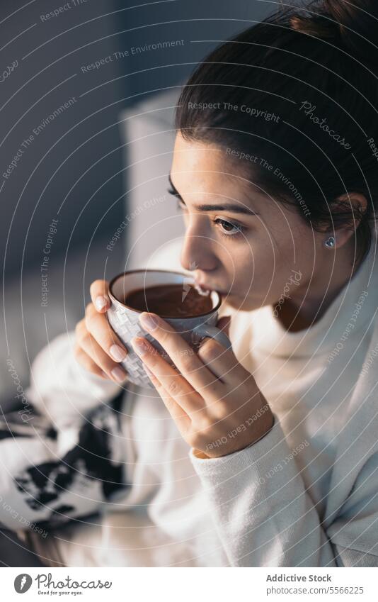Crop young woman sitting drinking coffee cup laptop using internet connection online living room at home female dark hair sofa gadget device beverage netbook