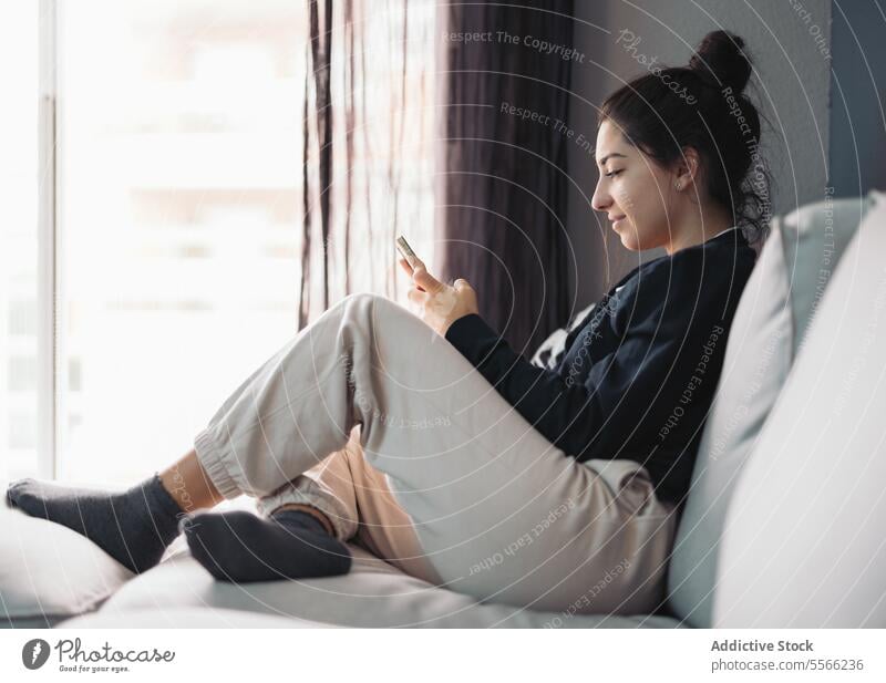 Happy young woman resting on sofa with smartphone using message relax online internet smile living room female sit browsing surfing gadget device mobile at home