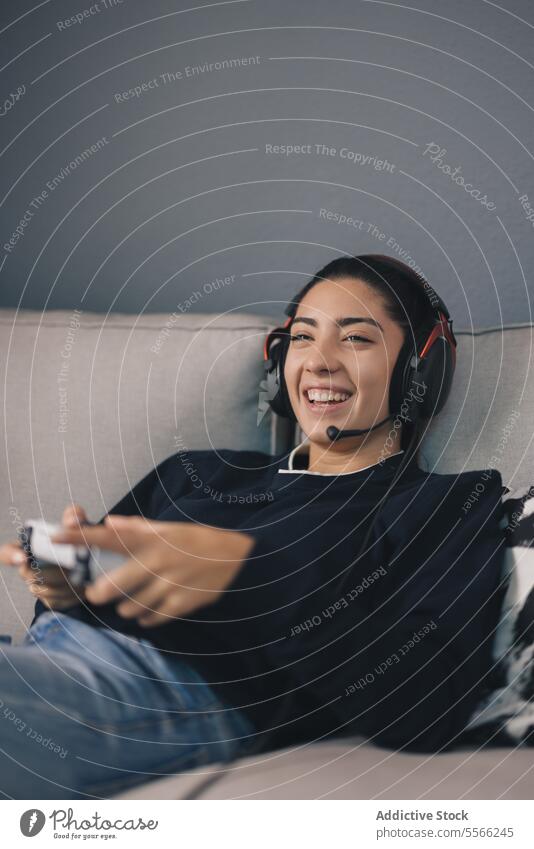 Smiling woman playing videogame with controller at home laugh joystick gamer sofa cheerful using console entertain headphones headset gadget smile device
