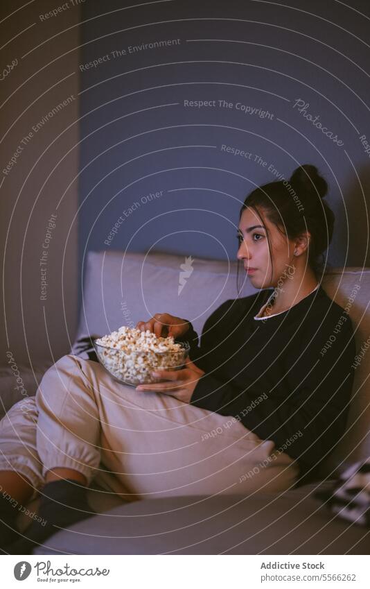 Young woman resting on comfortable sofa with popcorn bowl in living room relax sock light at home female young sit jacket sleeve cozy couch free time weekend