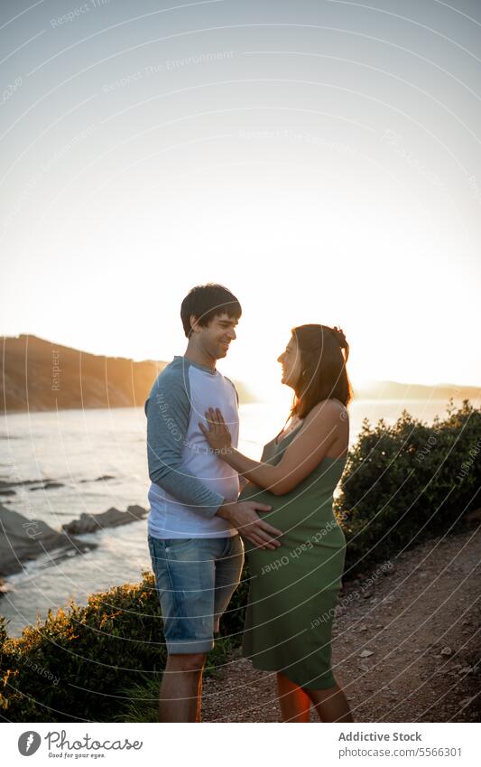 Happy pregnant couple standing together in nature hug pregnancy cliff love relationship happy man woman cheerful smile relax summer rest belly romantic tender