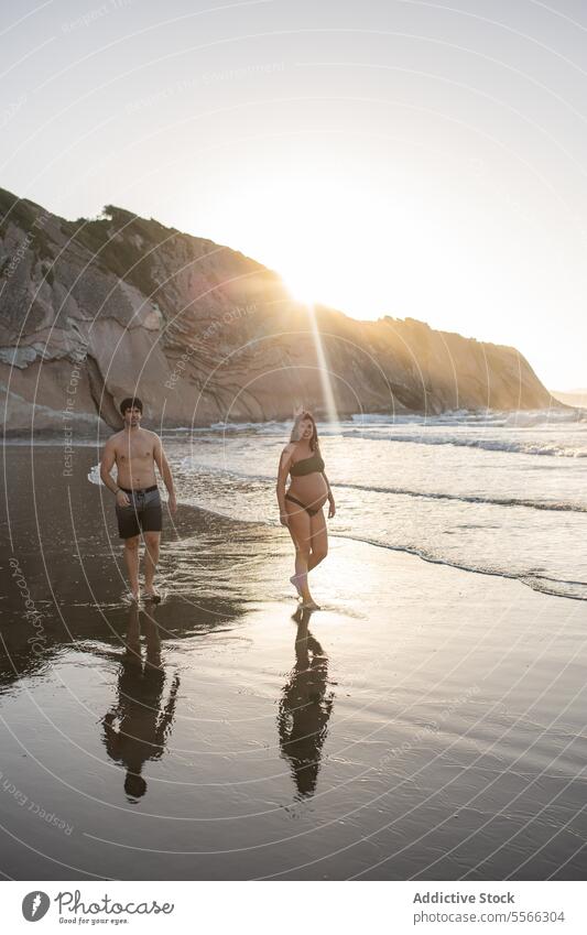 Pregnant couple walking near sea at sundown pregnancy together love coast relationship man woman shore pregnant mother parent father expect barefoot anticipate