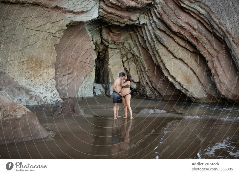 Pregnant couple kissing on seashore coast pregnant hug love relationship man woman embrace expect anticipate together vacation rest belly tender water maternal