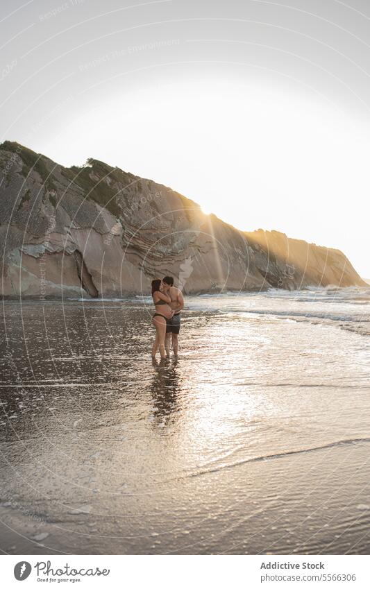 Pregnant couple kissing in sea in evening coast pregnant hug love relationship man woman embrace expect anticipate shore together vacation rest belly tender