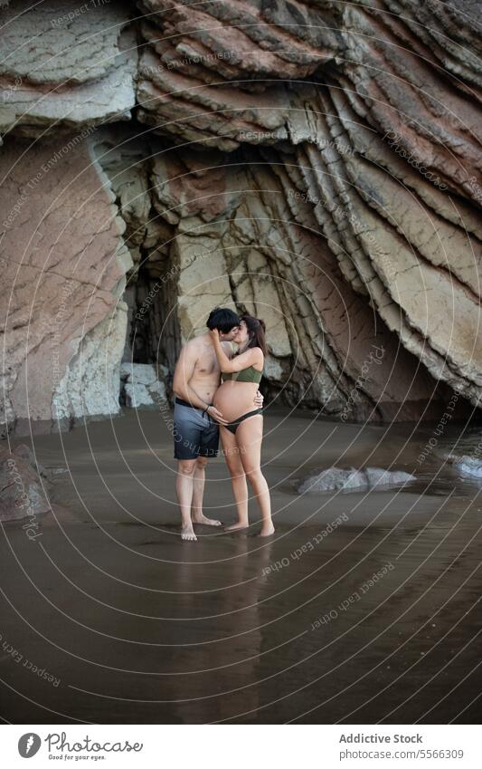 Pregnant couple kissing on seashore coast pregnant hug love relationship man woman embrace expect anticipate together vacation rest belly tender water maternal