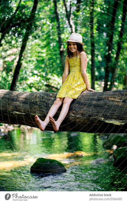 Cheerful preteen girl sitting on tree trunk in nature forest relax explorer break recreation adventure tranquil enjoy peaceful summer harmony freedom journey