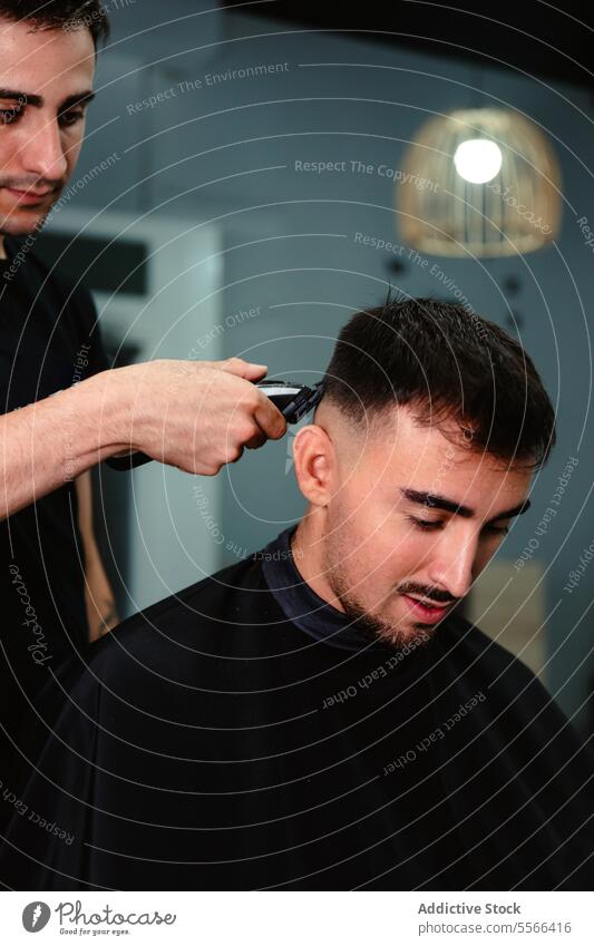 Young barber cutting a client's hair using an electric clipper. Barber trim young man salon light precision trimmer professional male caucasian style grooming