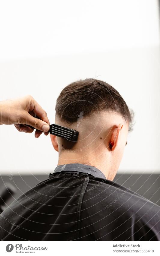 Focused view of a barber combing client's neatly trimmed hair. Close-up salon man grooming professional style short fade precision tool handle glide meticulous