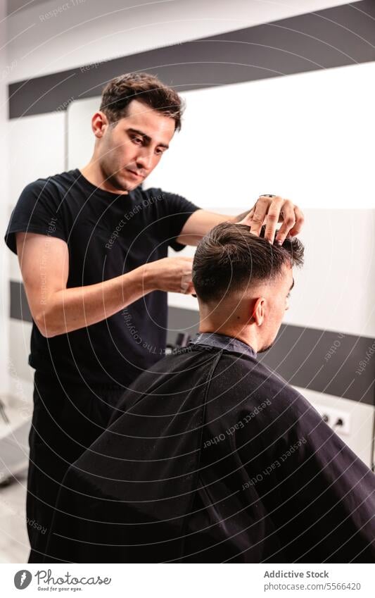 Young barber working in hair saloon. Barber scissors comb style salon white man focused attire black t-shirt hairdressing precision grooming cut professional
