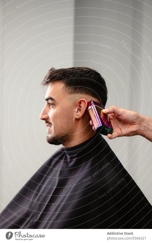 Barber using electric clippers for male client's hair trim. side profile precision care man grooming hand salon equipment styling modern young caucasian