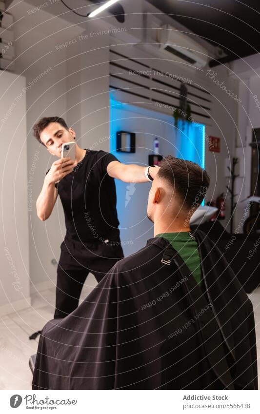 Barber capturing client's fresh hairstyle in lit salon photo black t-shirt man caucasian lighting contemporary phone camera capture modern interior smartphone
