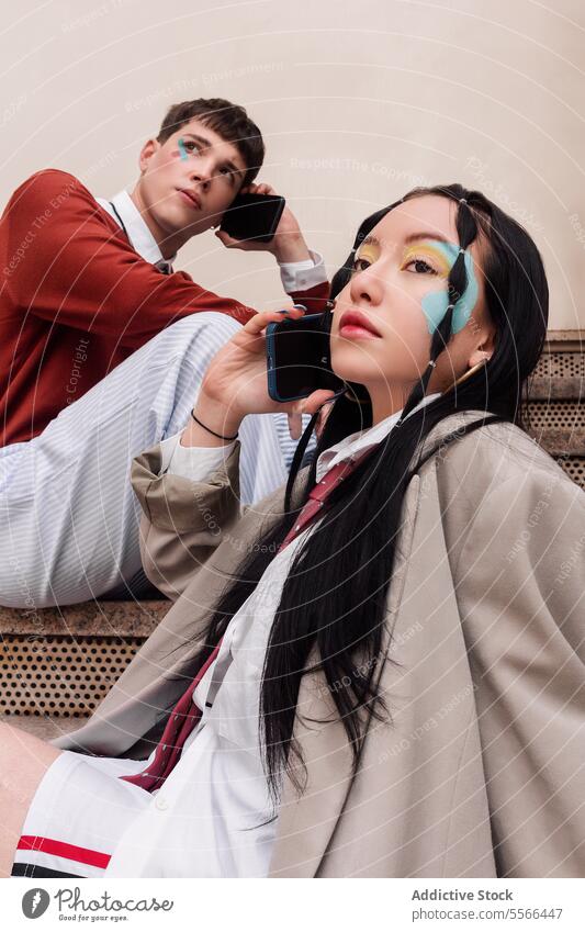 Gen-Z friends engrossed in smartphones with painted faces. Work concept. woman young work sitting stairs city youth makeup vibrant male female duo technology