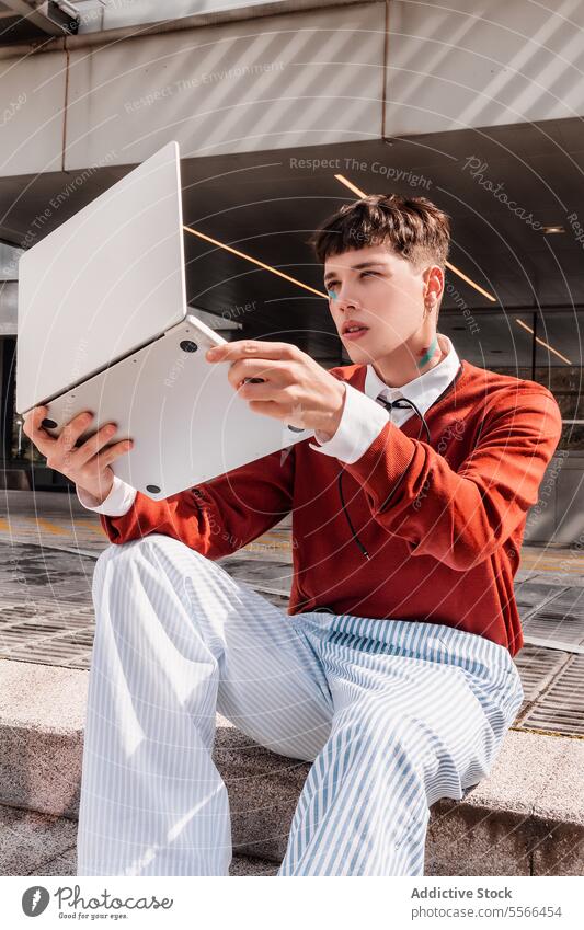 City young gen-z man lifting a laptop with his hand in fashion work concept. technology male outdoors architecture style sitting city urban digital device