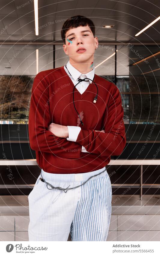 Stylish male model with connection cable around his neck paint at the entrance of a building. Male concept work gen-z face trendy young stand red sweater style