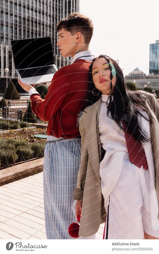 Portrait of Gen-Z duo in chic fashion with laptop and cup in city building background. Work concept. Fashion work outdoors male female makeup stylish urban
