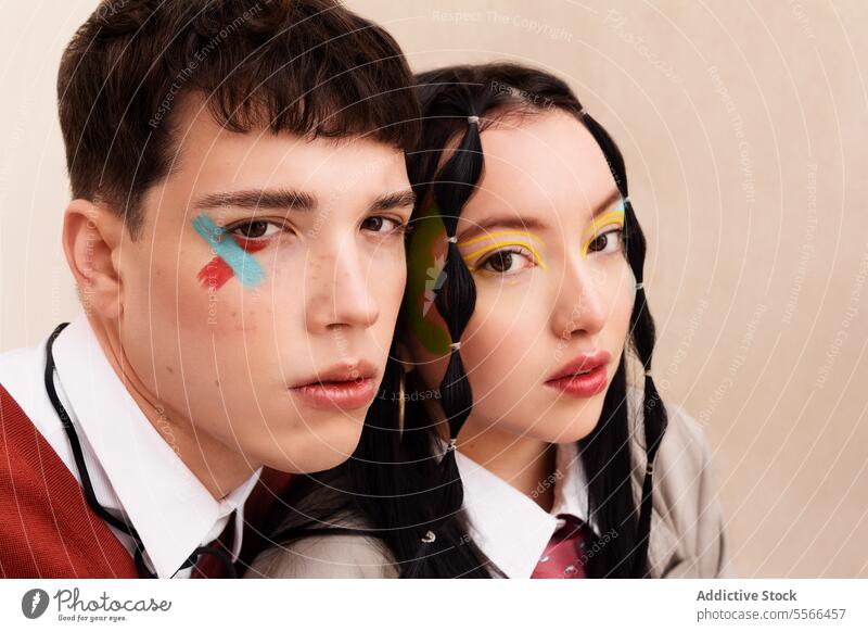 Close-up view of a young man and young woman showcasing bold colored makeup looking at front. Youth gen-z close-up face portrait male female fashion work style