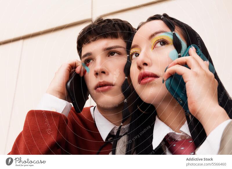 Young pair with vibrant makeup on call. Youth gen-z smartphone connection duo fashion outdoor conversation mobile contemporary style male female copy space