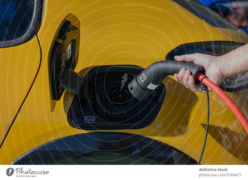 Anonymous person standing inserting charging power cable to electric vehicle at gas station charger car ecology transport energy auto modern eco friendly