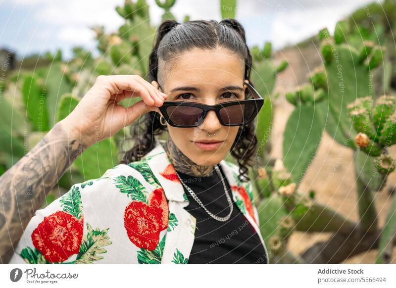 Tattooed woman standing on blurred cactus while adjusting sunglasses stylish nature tattoo attractive young fashion female pretty style cool beauty trendy