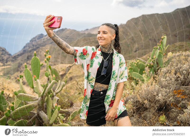 Tattooed woman taking selfie against mountains stylish nature tattoo standing attractive young fashion female pretty style cool beauty trendy casual modern cute