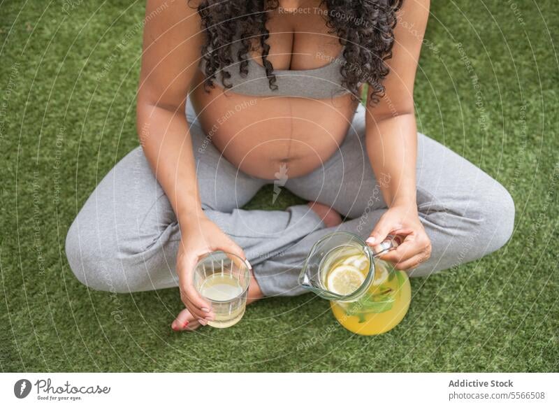 Pregnant woman enjoying a healthy drink outdoors pregnancy grass jug glass pouring refreshment sitting leisure relaxation nature nutrition maternity motherhood