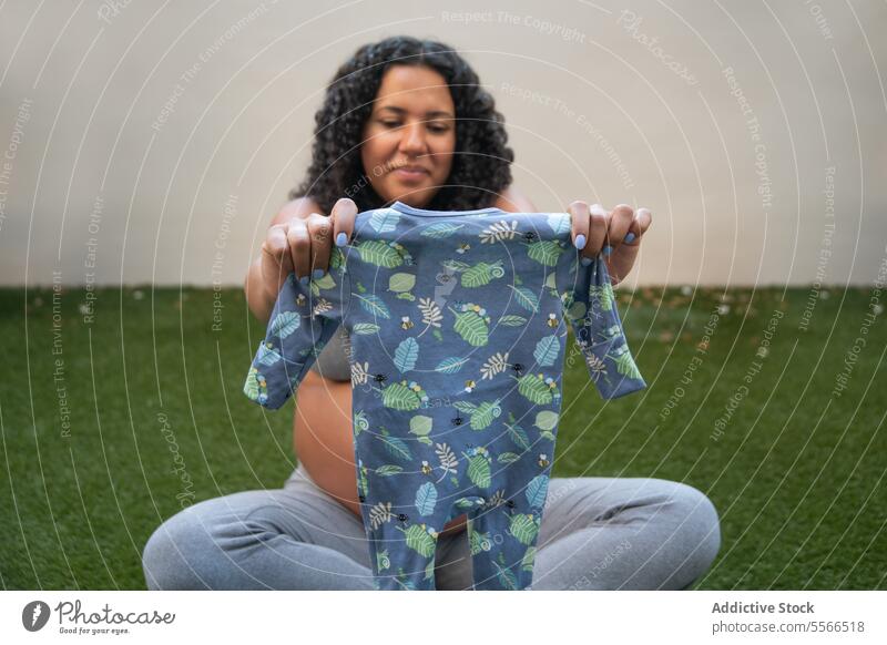Expectant mother showcasing baby onesie outdoors pregnancy expectant nature pattern blue joy anticipation clothing garden female maternity curly hair grass wall