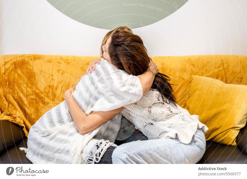 Two women sitting on a sofa while hugging each other woman couch covered blanket psychological therapy emotional relaxation comfort cozy home living room