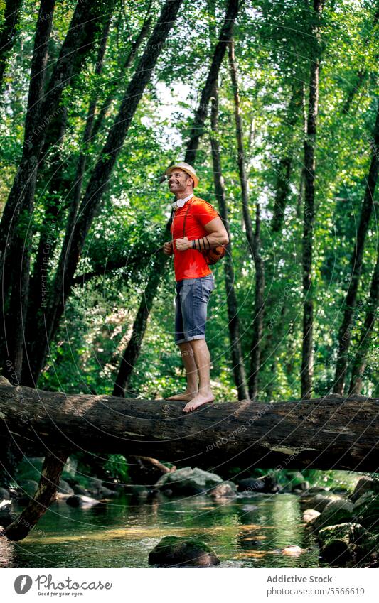 Hiker smiling man on a fallen log in lush green forest. hiker stand confident traveler happy looking accomplishment nature tree water backpack serene cheerful