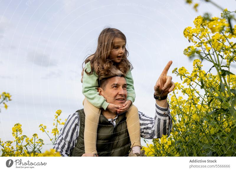 Dad pointing out sky wonders to his young daughter. father field flower bond family yellow attention curiosity nature parent child love outdoor together bloom