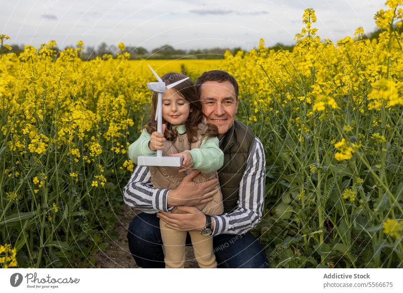Father-daughter embrace with windmill toy in field. father flower hug yellow bond love family nature miniature joy smile child outdoor meadow learning
