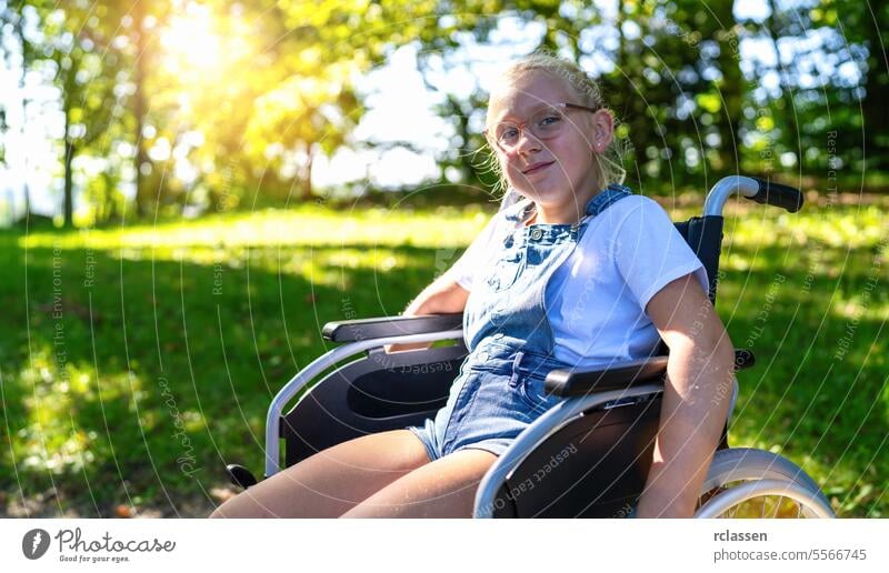 Happy young handicapped blond girl sit in wheelchair during walk in park, young disabled teenager in invalid carriage or wheel chair, young disability concept image
