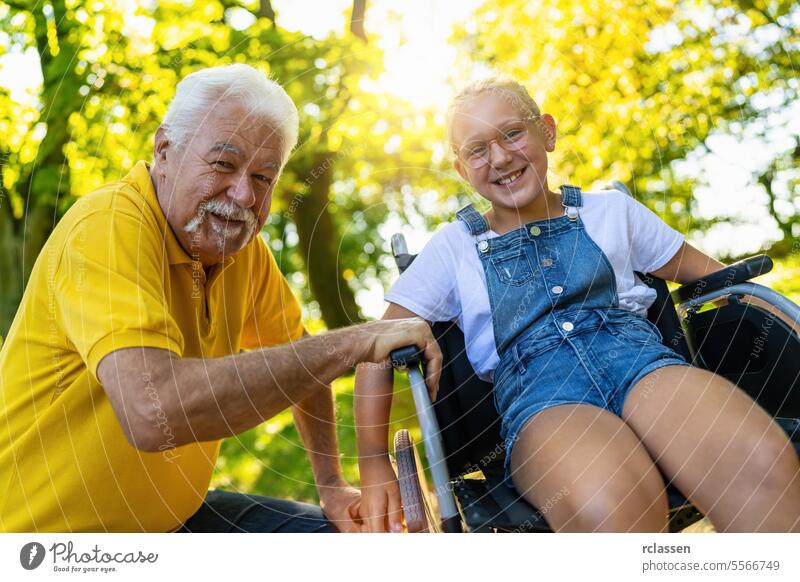 Happy grandfather and Granddaughter in wheelcahir taking a walk in the park at summer woman girl granddaughter wheelchair bonding family nature smiles happiness