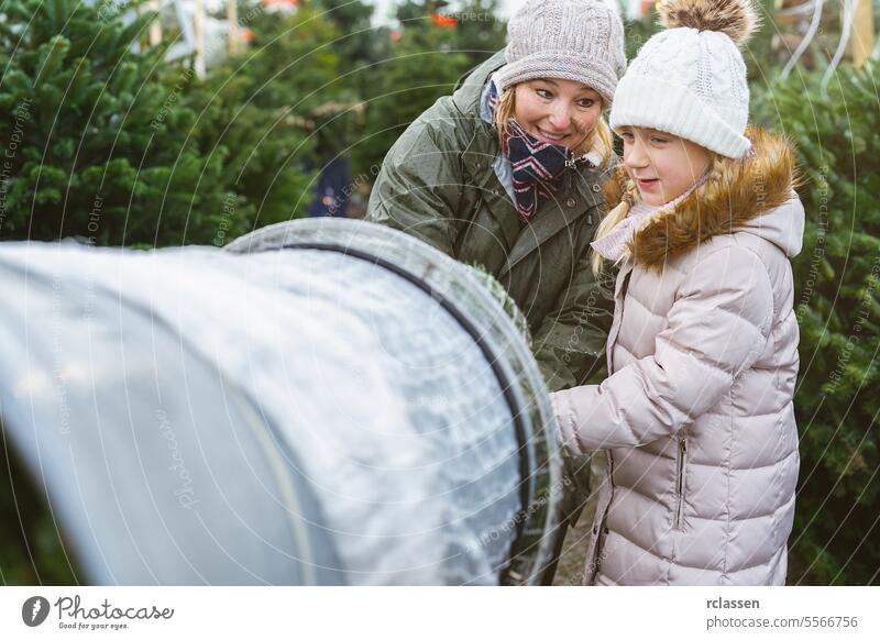 Happy saleswoman helpf a child being wrapped up a cut Christmas tree packed in a plastic net at a christmas market, Teamwork concept image teamwork buy daughter