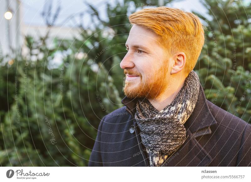 redhead man looks sideways amidst christmas trees on a street market genuine laughter joyful expression coat smile happiness looking surprised family happy